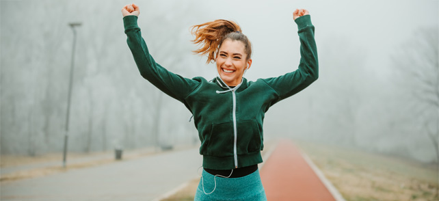 Futó nő kezeit feltartva örül a futópályán.