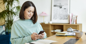 Fiatal barna hajú nő a telefonját nyomkodja.