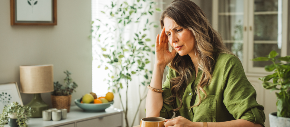 Középkorú nő, fáradtan ül a konyhaasztalnál.