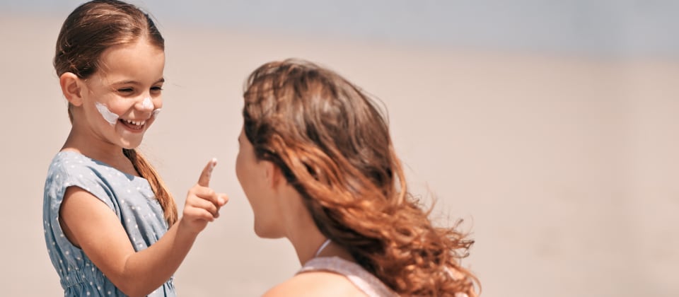 Kislány fényvédőt ken az anyukája arcára a strandon
